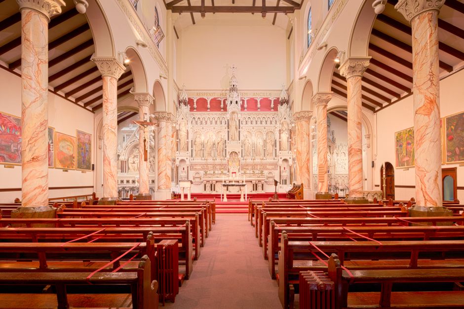 Inside St Johns Church, an ornate interior with high vaulted ceilings and detailed white and gold architectural features. At the front, a large, elaborate white altar with intricate carvings and statu