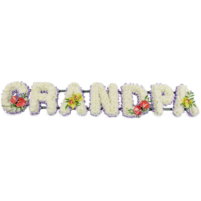 In this thoughtful funeral display, the word "GRANDPA" is presented in seven bold, upright letters arranged in a straight band, all set against a simple white backdrop that draws attention to colour and form. Each letter is made from a firm frame and smothered in small white chrysanthemums, placed so densely that they form one unbroken cushion of petals. The repeated texture of the chrysanthemums gives the tribute a calm rhythm, while their clean white tone symbolises peace and gentle remembrance. Along the bottom edge of each letter runs a fine line of pale lavender ribbon, offering a soft pastel contrast and a sense of careful craftsmanship, as though each letter has been gently underlined. Although the letters are fixed to a dark green support bar, the mechanics are mostly hidden beneath the flowers, allowing the eye to linger on the name itself. Four of the letters carry additional sprays of flowers that bring personality and depth: the "G" and the "D" feature structured groups of deep red anthuriums, their glossy, heart-shaped blooms and bright central spadices resting amid lush green foliage and occasional hints of smaller filler flowers. The first "A" and the final "A" are accented with graceful yellow-green orchids, their refined petals and slim stems sitting light and airy on the white background. The arrangement feels composed and heartfelt, the kind of tailored name tribute families in Upper Clapton might order for a funeral at a local church or crematorium, or for a service near Clapton Pond. It serves as a quiet statement of respect, a floral reminder of a grandfather's steady presence in the life of his family.