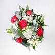 A hand-tied bouquet viewed from above, overflowing with crimson roses, pink-red carnations, and snow-white daisies that seem to glow against a backdrop of lush, deep green foliage. The roses are full and velvety, their petals spiralling inward like little hearts, while the carnations ruffle outwards with feathery edges that catch the light. Clusters of tiny white chrysanthemums and gypsophila, or baby's breath, form soft clouds between the bolder blooms, giving the arrangement a gentle, airy brightness. Eucalyptus stems arc gracefully through the bouquet, their cool grey-green leaves adding a modern touch and a faint herbal scent that you can almost imagine drifting across a living room in Upper Clapton. Behind them, glossy tropical leaves provide structure and depth, cradling the flowers so the reds and whites stand out clearly. The composition is round and balanced rather than stiff, suggesting the relaxed elegance of a bouquet delivered to a townhouse near Springfield Park for a birthday brunch or a surprise welcome home. Light falls from one side, picking up the satin sheen on the rose petals and the soft texture of the daisies, giving the whole piece a feeling of early morning optimism. Each flower appears freshly cut, with no bruising or fading, as if the stems have just been arranged by an experienced local florist who understands how to combine colour, fragrance, and texture into one harmonious gesture of affection. This is a bouquet that feels both celebratory and comforting, ideal for marking milestones or simply brightening a favourite corner of a home in E5.